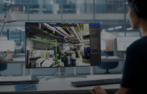 Person working at a computer displaying a detailed industrial digital twin in Prevu3D, with pipes and equipment highlighted on the monitor.