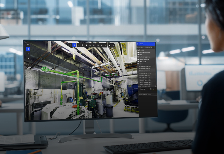User analyzing a 3D facility scan using RealityPlatform™ software on a widescreen monitor, highlighting industrial pipes and equipment.