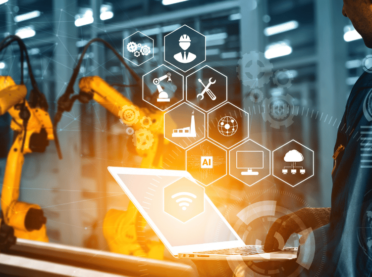 Engineer using laptop to monitor robotic arms and smart factory technology icons in an industrial setting
