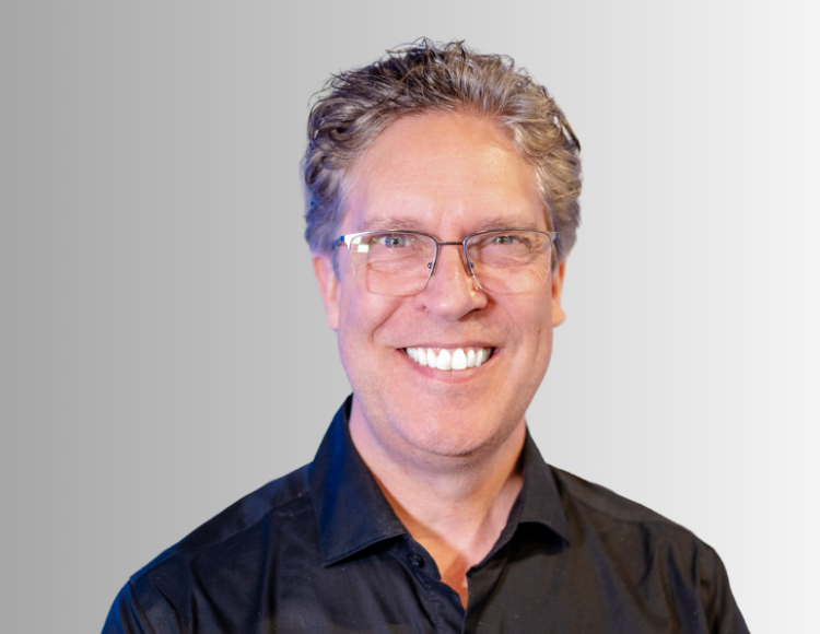 Portrait of Michel Besner, CEO of Prevu3D, smiling and wearing glasses and a black shirt, in front of a light gradient background.