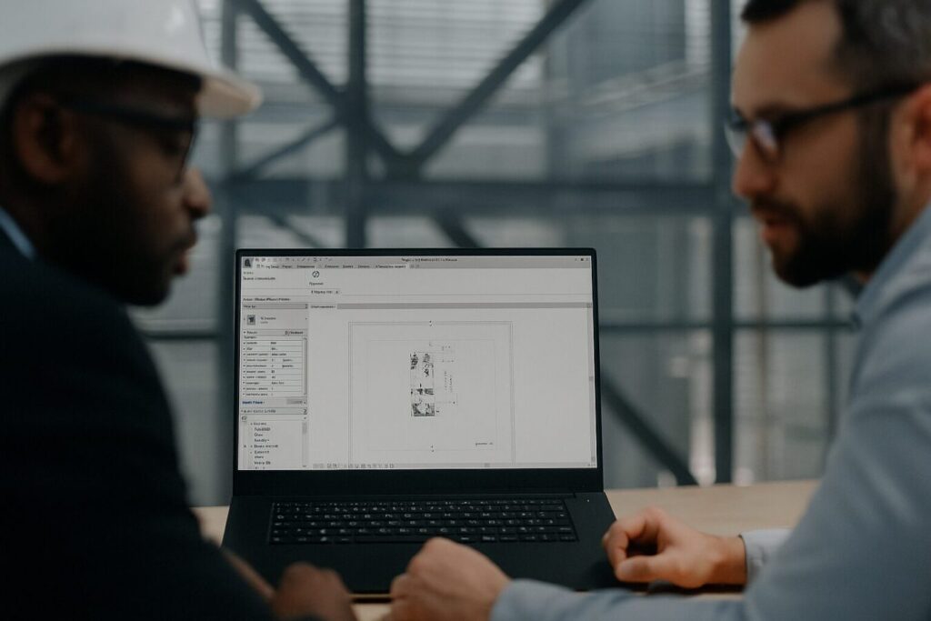 Two professionals reviewing a floor plan on a laptop using RealityConnect in an industrial office setting, with the users slightly blurred in the foreground.