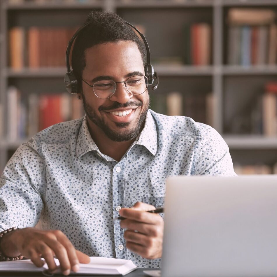 Smiling man attending a virtual webinar from home, wearing a headset and taking notes.