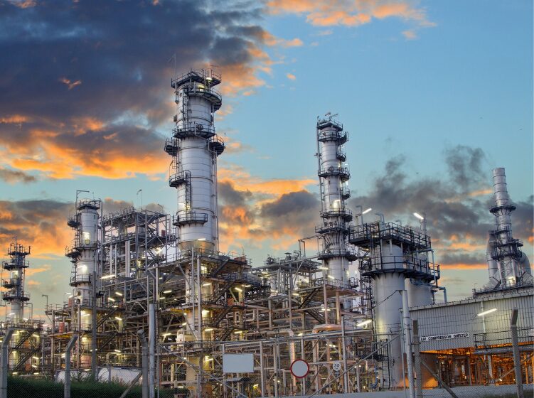 Oil and gas refinery facility at sunset with industrial towers and pipelines.