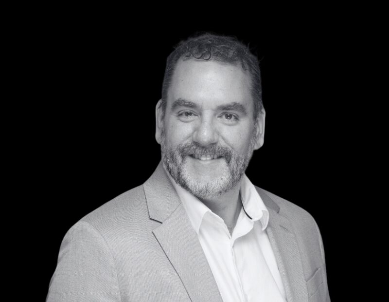 Portrait of Éric Lalancette, Head of Sales at Prevu3D, smiling and wearing a light-colored blazer and white shirt against a solid black background.”