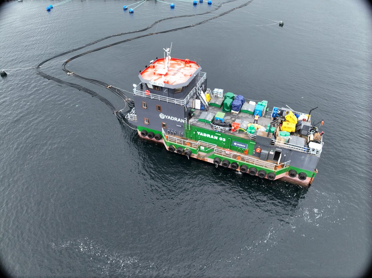 Workboat docked beside a floating fish farm installation, carrying equipment and supplies on deck