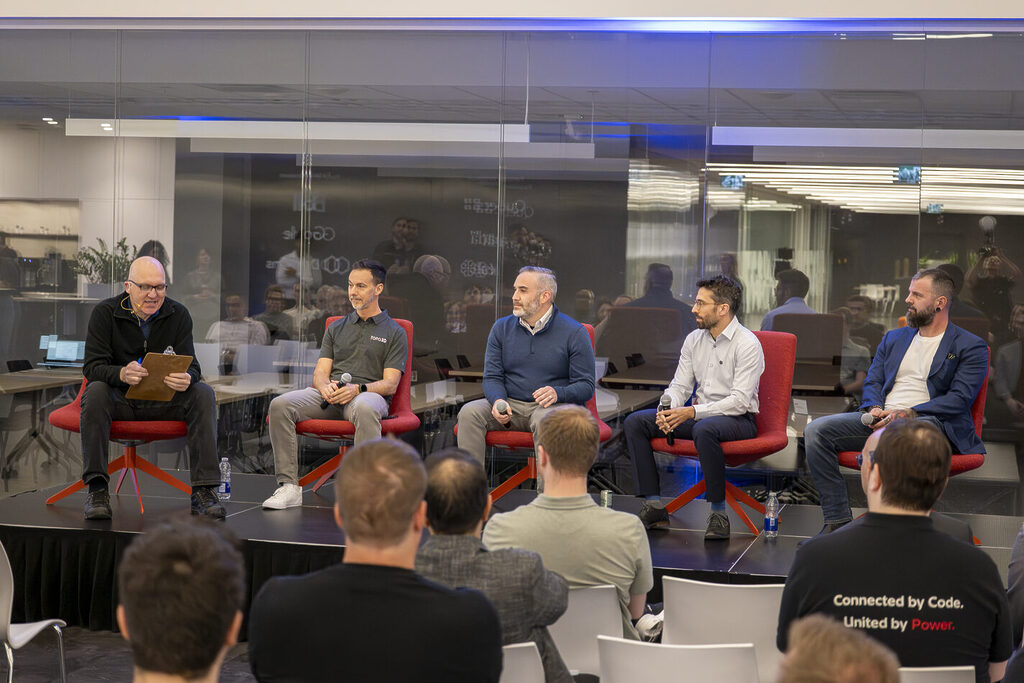 connexion 2026 panelists | prevu3d Panel discussion with five men seated on red chairs on a stage, microphones in hand, addressing an audience in a glass-walled room.