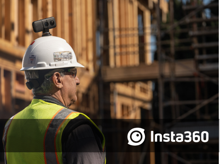 Construction worker wearing a hard hat and hi-vis vest with a mounted action camera on the helmet at a building site under construction.