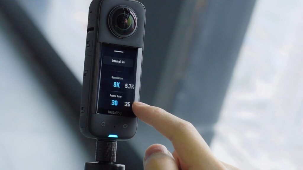 Hand taps the Insta360 action camera's touchscreen, showing 8K resolution and frame rate options on the display.