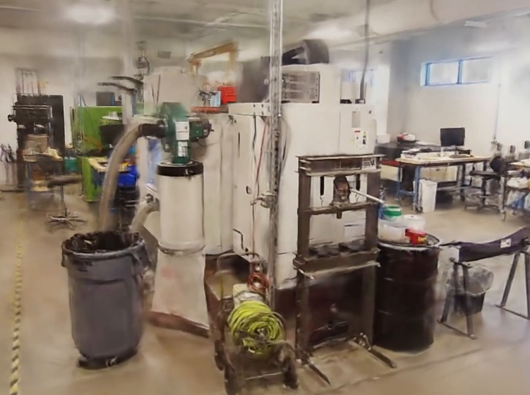 Industrial Workshop with Large Machinery and Workstations Foreground Shows a Trash Can Hoses and a Hydraulic Press While Desks and a Computer Sit in the Background Prevu3d